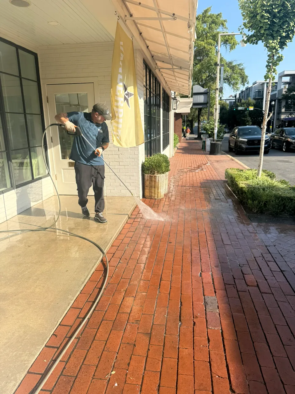 Operator washing a red-brick sidewalk outside a storefront with a yellow Vanderbilt banner