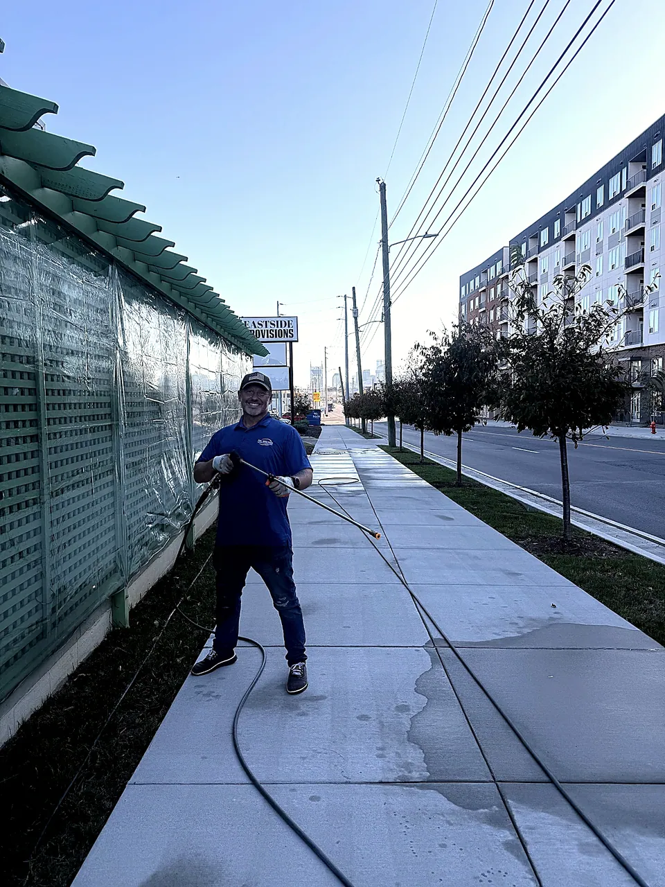FullSpectrumX operator smiling with a pressure-washing wand beside an urban sidewalk