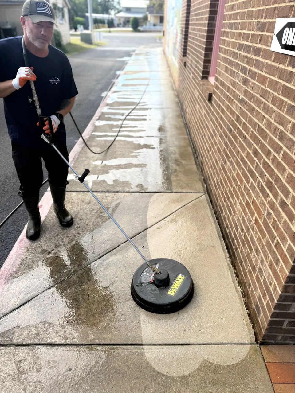 Pressure-washing surface cleaner and wand on a wet sidewalk beside a brick storefront